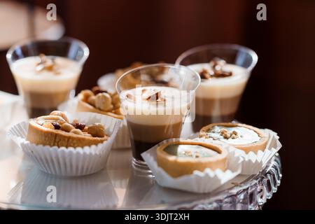 Una lussuosa varietà di dessert a base di mousse di caffè in bicchieri chiari e piccole tartette condite con noci, presentati su un piatto di cristallo riflettente con caldo Foto Stock