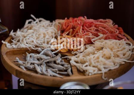Un piatto di legno splendidamente disposto mostra un assortimento di pesce secco che include filamenti di pesce bianco, gamberi rossi vibranti, arachidi dorate e SM Foto Stock