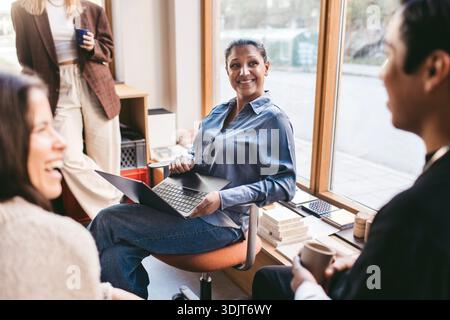 Donna d'affari sorridente e matura seduta con un laptop durante una riunione in un nuovo ufficio Foto Stock