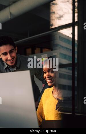 Programmatore donna sorridente che utilizza il computer mentre lavora con un collega maschio nell'ufficio tecnico Foto Stock