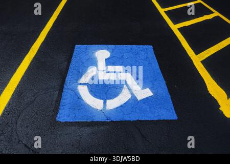 Simbolo dello spazio di parcheggio accessibile con sedia a rotelle verniciato sulla superficie dell'asfalto. Segnaletica blu di parcheggio per disabili con icona sedia a rotelle su strada. Infrastrutture urbane. Foto Stock