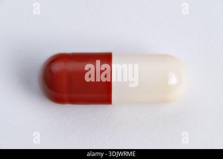 primo piano di una capsula singola rossa e bianca che mette in risalto la superficie lucida e la cucitura, foto di un prodotto macro per il branding e il confezionamento, isolata su un backgrou neutro Foto Stock