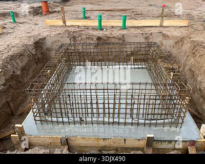 Basamento in cemento armato in costruzione con una gabbia di armatura in acciaio posizionata all'interno di una fossa di fondazione scavata. L'immagine mostra una lastra di base in calcestruzzo Foto Stock