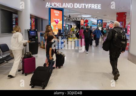 I viaggiatori con bagagli rotanti attraversano Auckland Duty Free all'interno dell'aeroporto di Auckland, nuova Zelanda, passando davanti a espositori e segnaletica. Foto Stock