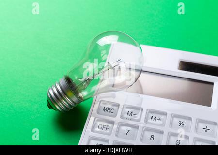Calcolatrice con lampadina a incandescenza su sfondo verde. Piatto a risparmio energetico Foto Stock