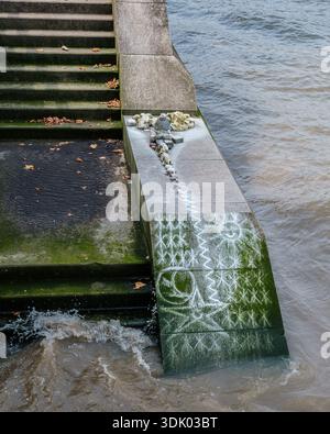 Disegni di gesso e pietre disposte su gradini di pietra usurati ai margini del Tamigi, mostrando acqua di marea e crescita di alghe. Foto Stock