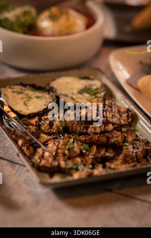 Verdure miste grigliate condite con formaggio fuso ed erbe fresche, servite su un piatto rustico in una presentazione gastronomica in stile ristorante Foto Stock