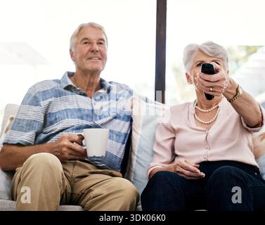 Caffè, relax e coppia di anziani che guardano la tv a casa per intrattenimento, film o programmi in pensione. Tè, donna anziana e uomo con televisore nella sala Foto Stock