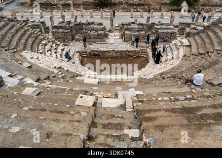 Selcuk, Smirne, Turchia - 4 febbraio 2025: I turisti esplorano le antiche rovine del teatro Odeon a Efeso, con scalini in pietra, un'orchestra e colonne sparse sotto un cielo coperto Foto Stock