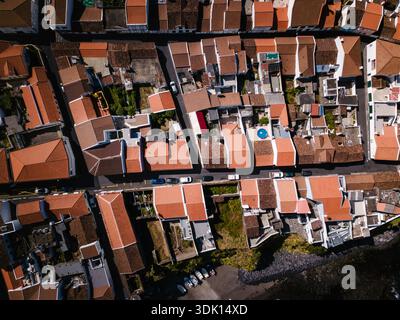 Vista aerea dall'alto verso il basso di una fitta città costiera sulle Azzorre. Tetti di tegole rosse, stradine strette, auto parcheggiate, piccoli cortili e la costa rocciosa della E. Foto Stock