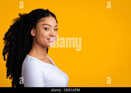 Donna afroamericana sorridente con capelli ricci in posa su sfondo giallo Foto Stock