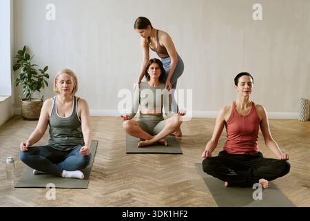 Gruppo di donne di mezza età che praticano Yoga con istruttore per giovani adulti Foto Stock