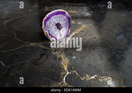 Geode di agata tinta con formazione visibile di cristallo di quarzo, fotografato su una superficie di marmo scuro con luce direzionale soffusa. Foto Stock