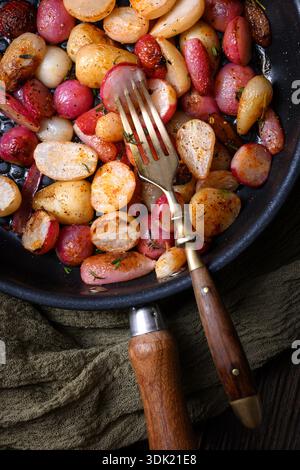 Ravanelli al forno con erbe in padella nera con posate vintage. Piatto di verdure salate per mangiare pulito e atmosfera rustica da cucina Foto Stock
