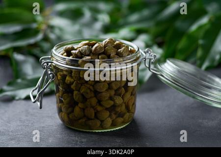 Capperi commestibili in vaso di vetro pronti da mangiare su sfondo di marmo nero, messa a fuoco selettiva. Foto Stock