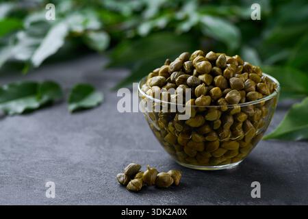 Capperi marinati in una ciotola di vetro pronti da mangiare su sfondo di marmo nero, messa a fuoco selettiva. Copia spazio per il testo. Foto Stock