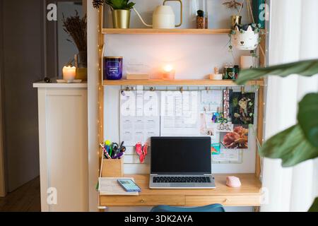 Stazione remota per piccoli uffici domestici, spazio di lavoro, con computer portatile, impianti domestici, pannello a parete e candele. Foto Stock