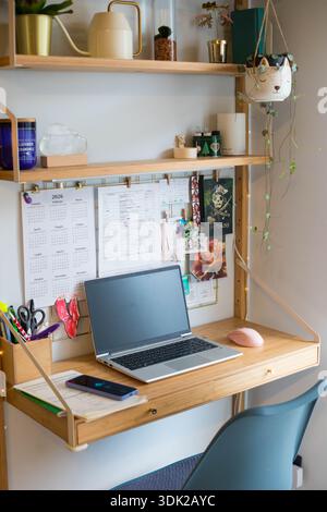 Stazione remota per piccoli uffici domestici, spazio di lavoro, con computer portatile, impianti domestici, pannello a parete e candele. Scatto verticale. Foto Stock