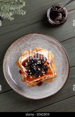Primo piano di due fette di pane leggero tostato e spalmato con formaggio spalmabile, ricoperto da un mucchio di more fresche, condite con marmellata o sciroppo, a. Foto Stock