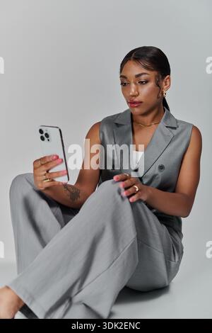 Una giovane donna elegante si siede in uno studio mentre utilizza il suo smartphone. Foto Stock