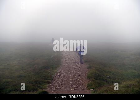 Due uomini anziani (escursionisti) camminando nella nebbia sul sentiero per la Wainwright 'Raise' vicino a Stanah, Thirlmere, Lake District National Park, Cumbria, Inghilterra, Regno Unito Foto Stock
