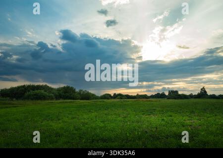 Il sole emerge da dietro una nuvola scura sopra un prato verde Foto Stock