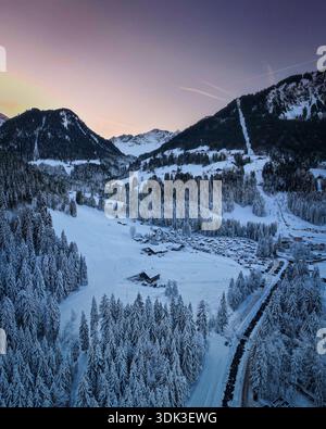 Vista aerea di pini e chalet innevati si annidano nella valle, con cime baciate dalla luce alpina che svanisce, Champéry, Vallese, Svizzera. Foto Stock