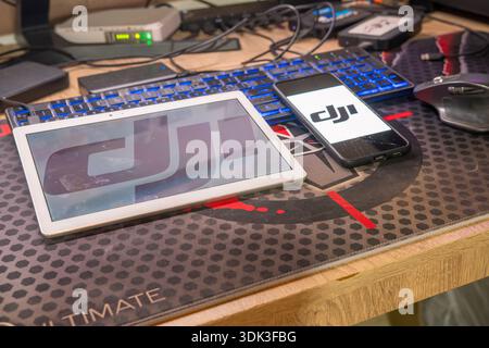 Tablet bianco e smartphone nero con logo DJI per l'applicazione Drone Flight Control appoggiata sulla superficie della scrivania del computer Foto Stock