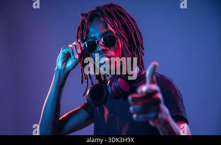 Puntando con il dito, con gli occhiali da sole. L'afroamericano è uno studio con illuminazione al neon. Foto Stock