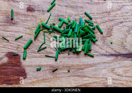 Erba cipollina fresca tritata o cipollotti sparsi su un rustico asse di legno. Ingrediente di erbe sano. Foto Stock