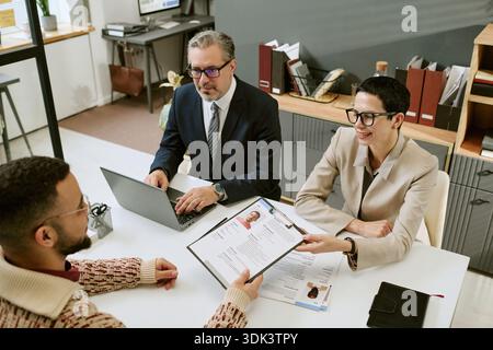 Uomo e donna di mezza età che intervistano l'uomo giovane adulto Foto Stock