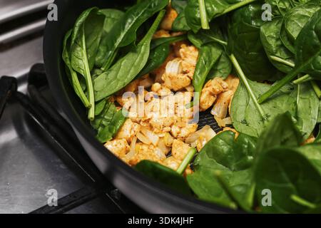 TITOLO: Cottura di spinaci e pollo in padella per friggere. Sana preparazione di pasti fatti in casa su piano cottura. Verdure verdi fresche con carne. Foto Stock