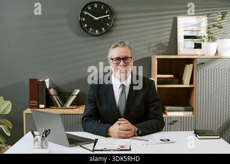 Ritratto di un uomo di mezza età sorridente mentre è seduto alla scrivania in ufficio Foto Stock
