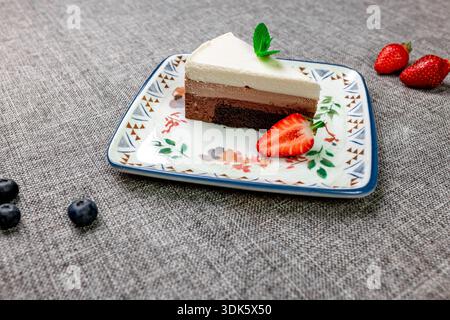 Squisito dessert a più strati, leggero e arioso "tre cioccolatini" su un piatto bianco a motivi geometrici. Uno scatto in primo piano verticale mostra la delicata texture Foto Stock
