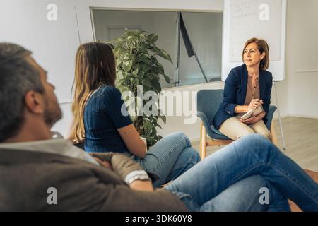 Una terapeuta professionista ascolta attentamente una giovane coppia durante una sessione di consulenza matrimoniale in un ufficio luminoso e moderno per migliorare il loro Foto Stock