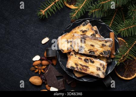 Fette di stollen tradizionale con marzapane, uvetta, ciliegie di glace e mandorle sono servite in una ciotola di metallo accanto a una tazza di caffè su una barba scura Foto Stock