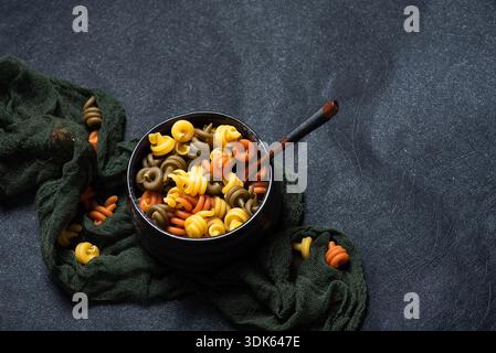 Pasta italiana tricolore, secca, non cotta in una ciotola di ceramica nera su sfondo nero. Trottole di pasta tricolore. Vista dall'alto Foto Stock