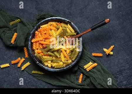 Pasta Fusilli tricolore cruda in una ciotola nera, su sfondo scuro. Vista dall'alto Foto Stock