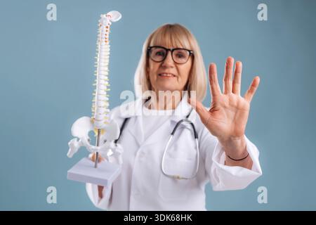 Ferma il gesto della mano, tenendo il modello della colonna vertebrale umana. Medico donna anziana è in background. Foto Stock