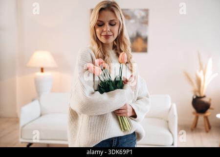 Felice espressione facciale. La bella giovane donna è a casa con i fiori. Foto Stock