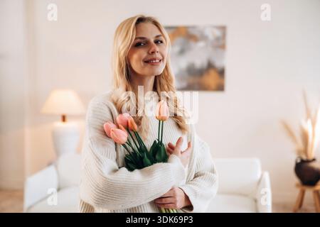 Felice espressione facciale. La bella giovane donna è a casa con i fiori. Foto Stock