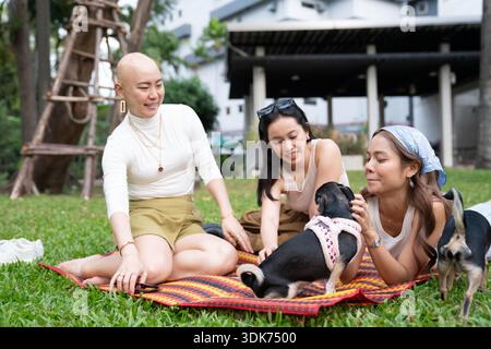 Amici che fanno un picnic nel parco con il cane, a sostegno di una donna calva Foto Stock