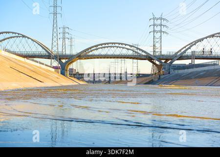 Il Viaduct Bridge della Sesta strada si affaccia sul fiume Los Angeles nel centro di Los ANGELES, con linee elettriche e argini in cemento sotto un cielo azzurro. Foto Stock