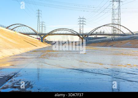 Il moderno ponte del viadotto della Sixth Street si estende sopra il canale di cemento del fiume Los Angeles sotto un cielo azzurro, mostrando le infrastrutture urbane e la città Foto Stock