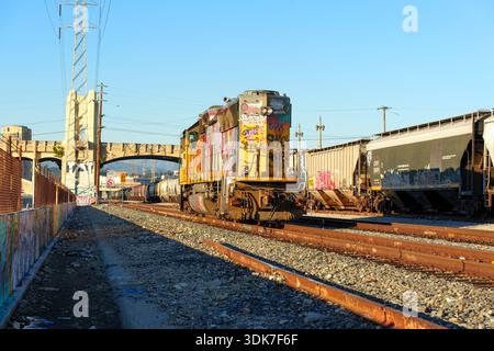 Los Angeles, California - 10 gennaio 2026: Treni merci gialli ricoperti di graffiti su binari, circondati da altri vagoni ferroviari e dagli imponenti sei Foto Stock