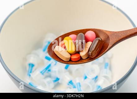 Concetto di scelta medica tra farmaci orali e iniezioni. Cucchiaio di legno pieno di pillole colorate e integratori su uno sfondo di molti utilizzati Foto Stock
