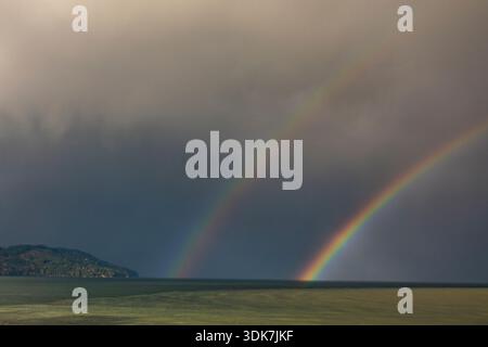 Un doppio arcobaleno in un cielo buio e tempestoso, che scende fino all'orizzonte. Foto Stock