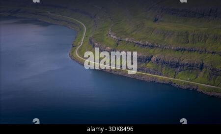 Vista aerea di una strada tortuosa che serpeggia lungo le ripide e verdi scogliere che contrastano con il mare blu profondo, Torshavn, Isole Faroe. Foto Stock