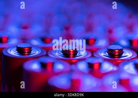 Primo piano delle estremità positive delle batterie scariche dimensioni AA, scatto macro, messa a fuoco selettiva. Batteria alcalina usata. Concetto di spazzatura pericolosa. Luce blu e rossa al neon Foto Stock
