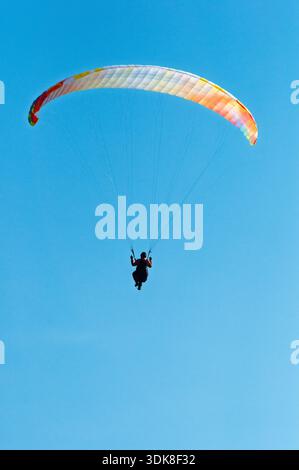 Un parapendio si libra attraverso un cielo azzurro, godendosi la libertà di volare. Foto Stock